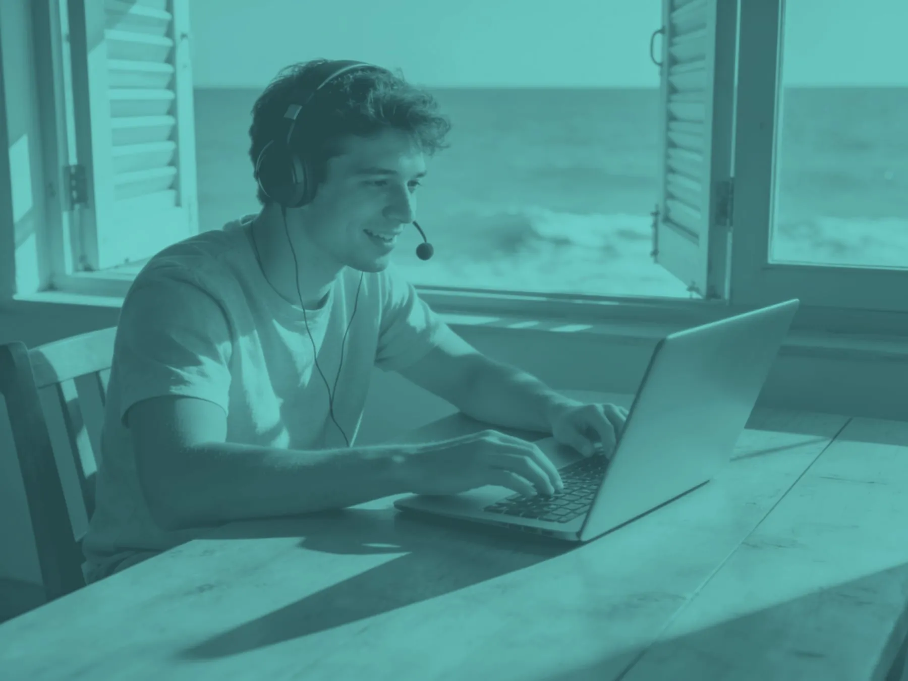A young man with a headset on a video call by an open window with the sea outside